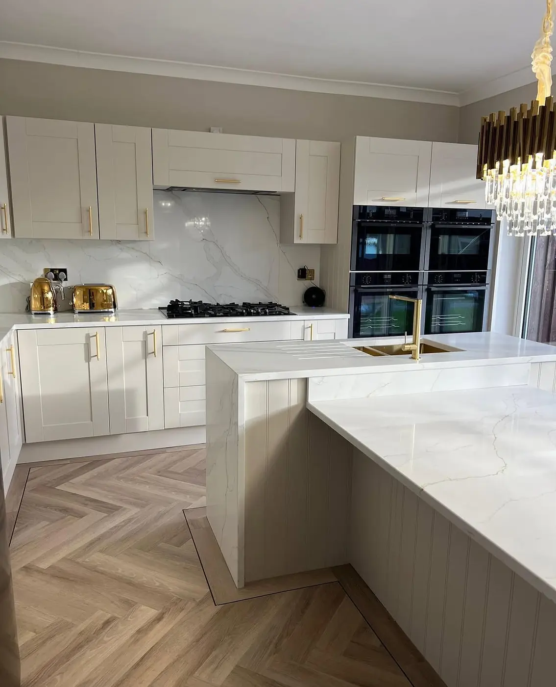 White kitchen island on herringbone flooring with brass fittings